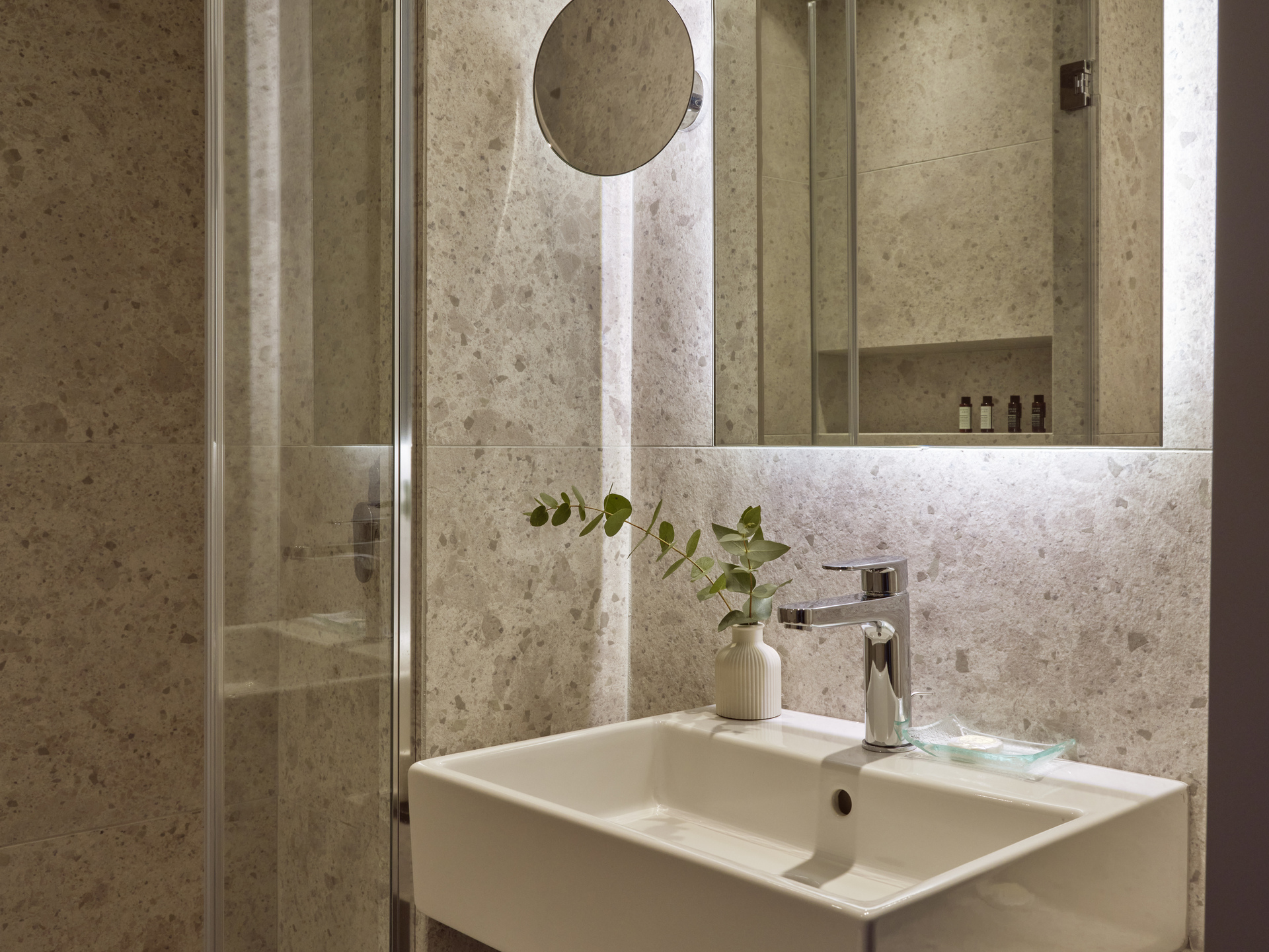 
Contemporary City Hotel bathroom with marble walls, glass shower, and minimalist sink area